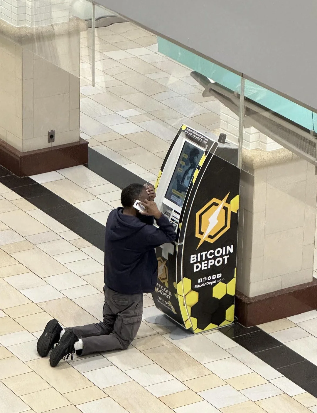 Person using a phone beside a Bitcoin Depot kiosk in an indoor public concourse