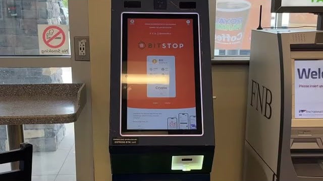 A Bitstop-branded Bitcoin ATM inside a Royal Farms convenience store, with a placard reading Owned and Operated by Express BTM LLC and a First National Bank traditional ATM visible beside it