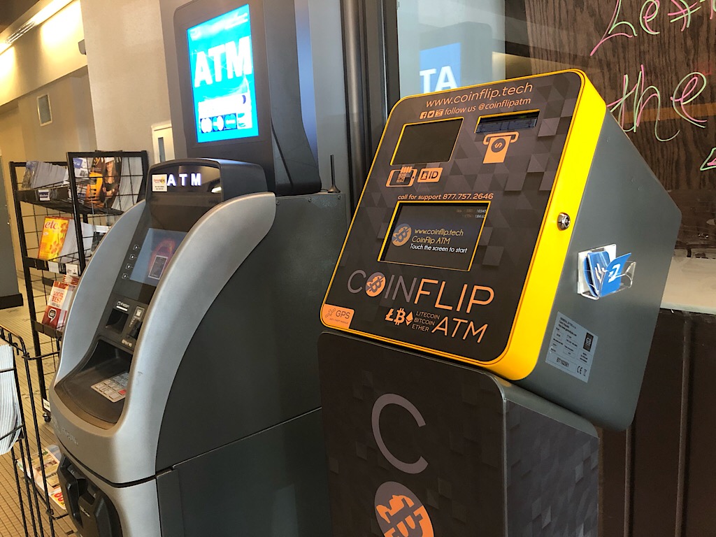 Yellow and black CoinFlip Bitcoin ATM deployed on a retail countertop next to a standard cash ATM