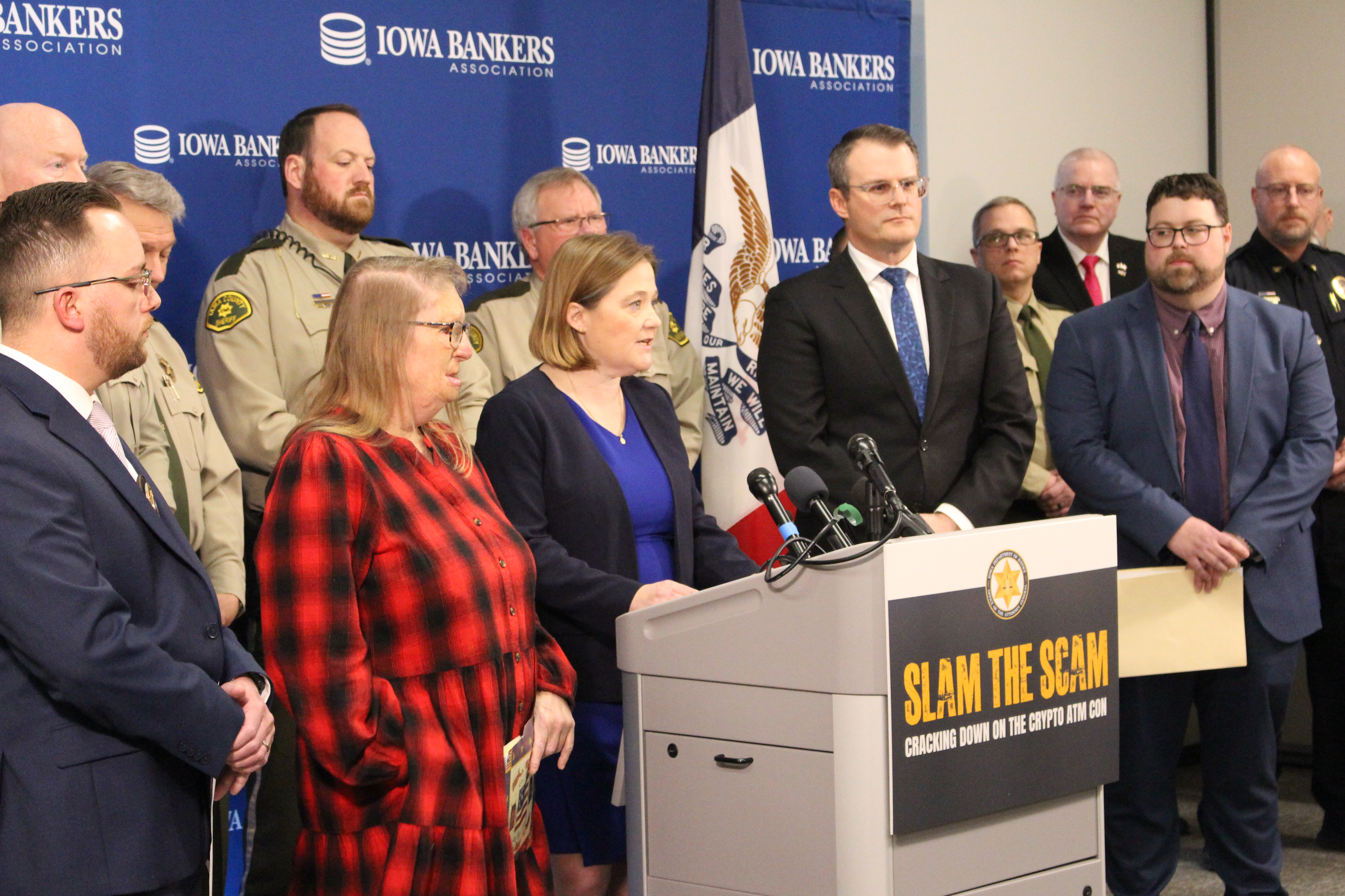 Iowa Attorney General Brenna Bird and other speakers at the February 26, 2025 press conference, with Iowa Bankers Association backdrop and a 'Slam the Scam — Cracking Down on the Crypto ATM Con' podium sign.